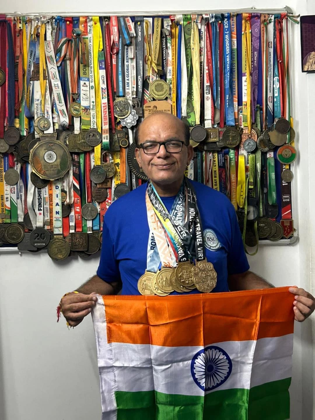 Gaurav Chaudhary, MilesToEarn's event ambassador, holding the Indian flag in front of his wall of marathon medals